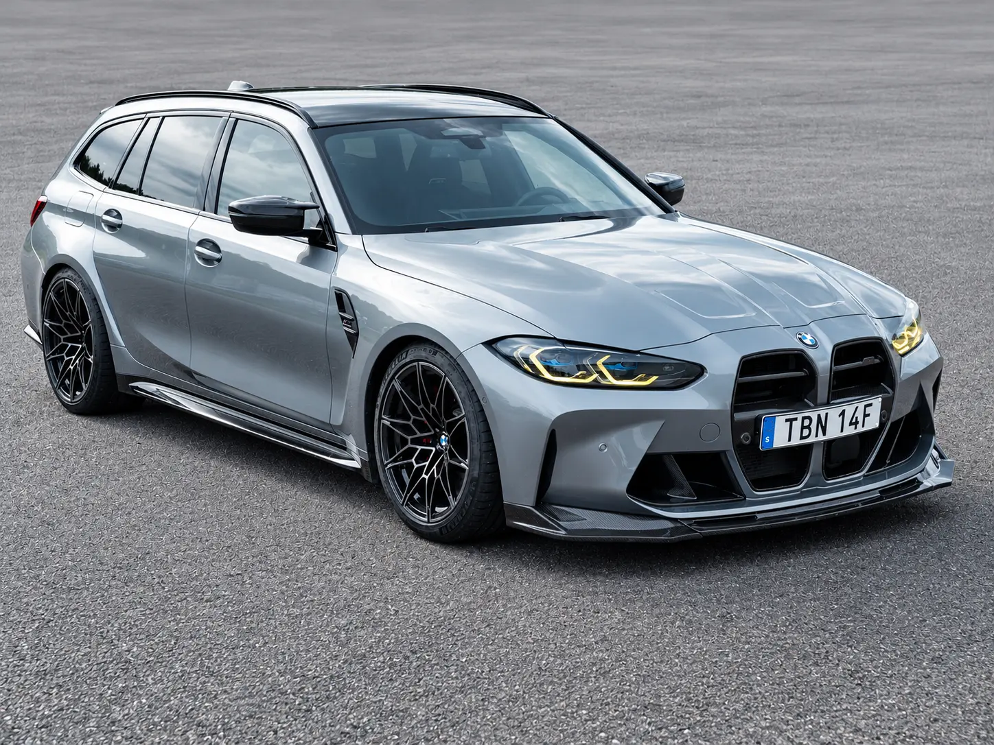 Metallgrå BMW M3 Touring med svarta fälgar på asfalt